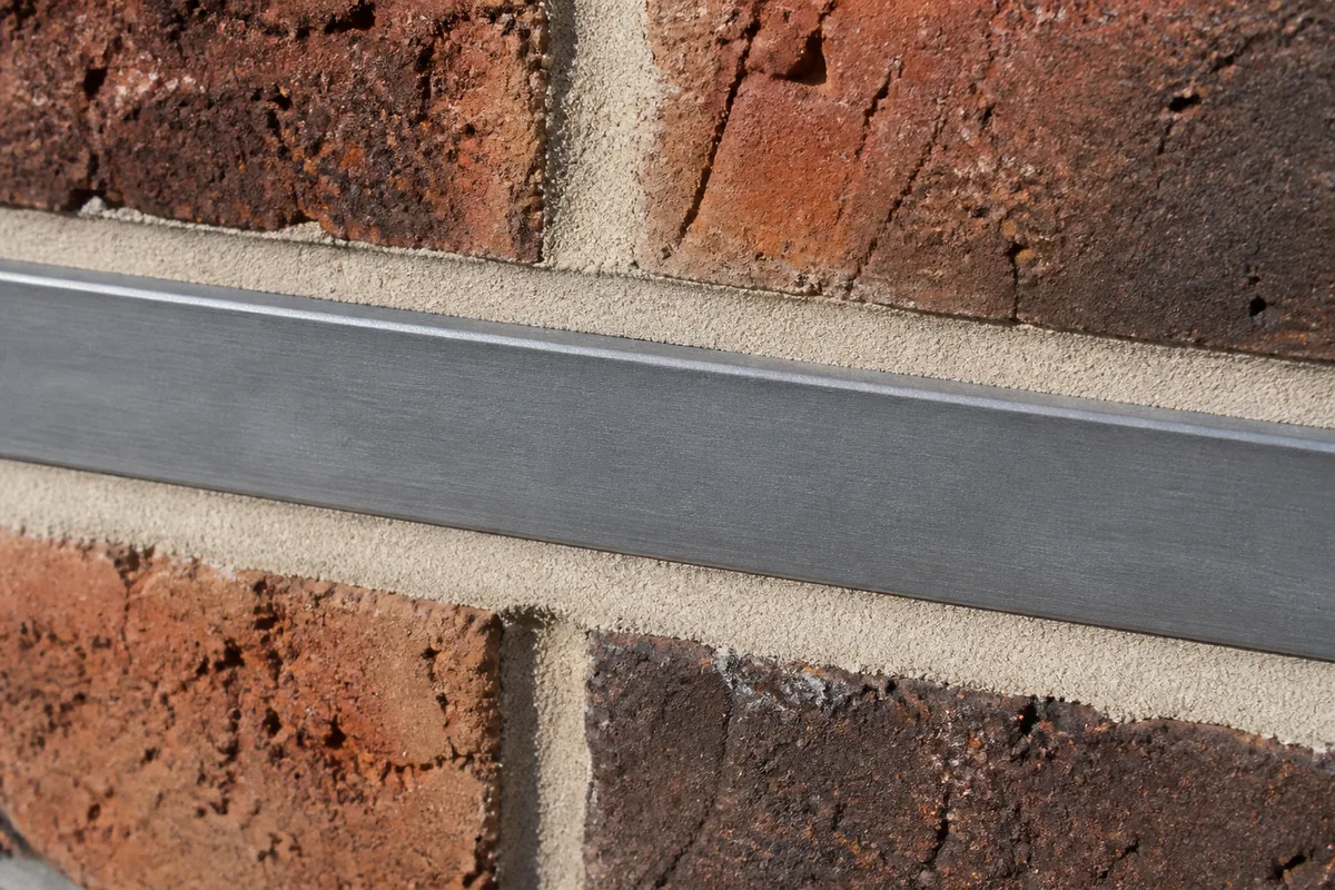 Détail d&rsquo;une engravure dans un mur de briques recevant le bord relevé d&rsquo;une bande de zinc